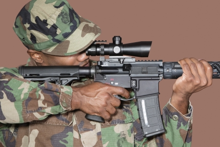 Male US Marine Corps soldier aiming M4 assault rifle over brown backgroundの写真素材