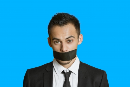 Portrait of a young businessman with adhesive tape on mouth over colored backgroundの写真素材