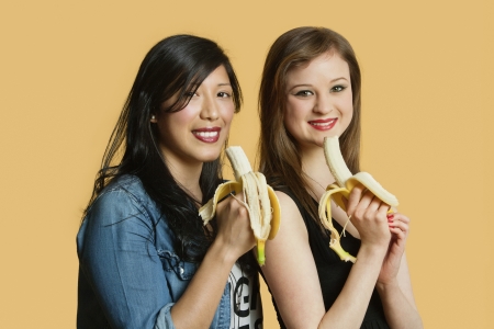 Portrait of female friends with banana over colored backgroundの写真素材