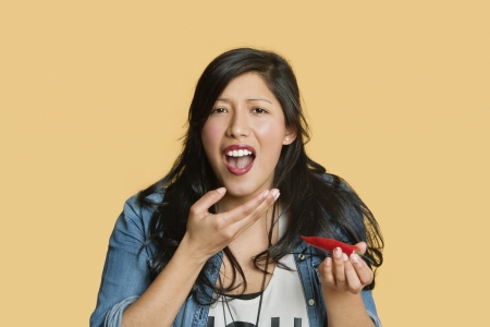 Portrait of a young woman eating red hot chili pepper over colored backgroundの写真素材