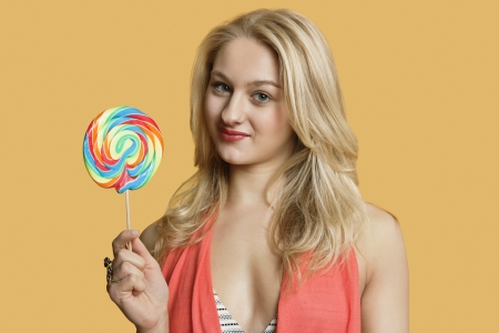 Portrait of a young blond woman holding lollipop over colored backgroundの写真素材