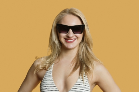 Portrait of a beautiful young woman in bikini wearing sunglasses over colored backgroundの写真素材
