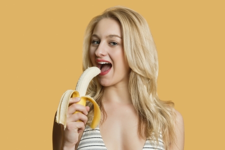 Portrait of a beautiful blond woman eating banana over colored backgroundの写真素材