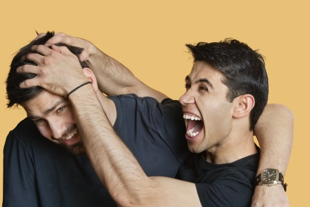 Young male friends playfighting over colored backgroundの写真素材