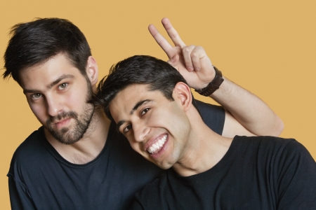 Portrait of young male friends with peace sign over colored backgroundの写真素材