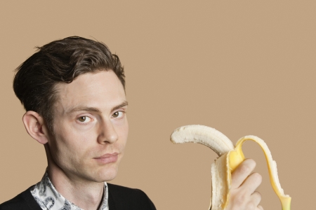 Portrait of a mid adult man holding banana over colored backgroundの写真素材