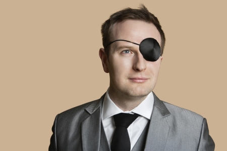 Close-up of a young businessman with eye patch looking away over colored backgroundの写真素材