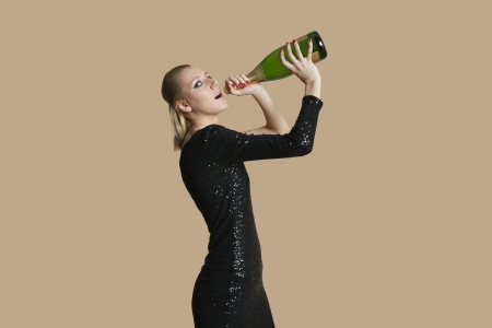 Portrait of beautiful young woman drinking champagne from bottle over colored backgroundの写真素材