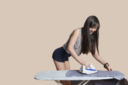 Young woman ironing shirt over colored backgroundの写真素材
