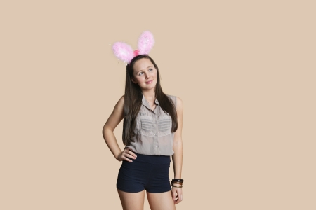 Beautiful young woman wearing rabbit ears while looking away over colored backgroundの写真素材