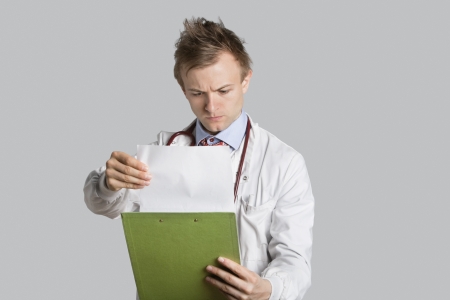 Male doctor reading medical records over gray backgroundの写真素材