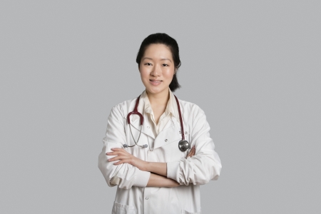Portrait of an Asian female doctor standing with arms crossed over gray backgroundの写真素材