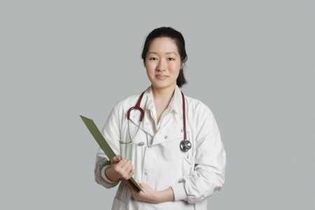 Portrait of an Asian female doctor holding a clipboard over gray backgroundの写真素材