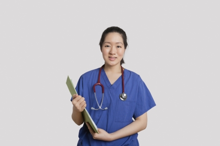 Portrait of an Asian female nurse holding clipboard over gray backgroundの写真素材
