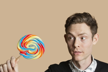 Mid adult man looking at lollipop over colored backgroundの写真素材