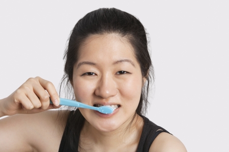 Portrait of a young woman brushing her teeth over light gray background