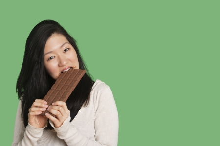 Portrait of a young woman eating a large chocolate bar over green backgroundの写真素材