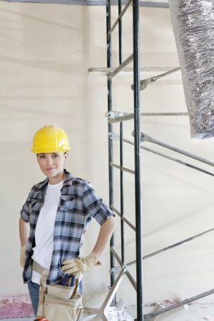 Portrait of mid adult woman standing with hands on hips at construction siteの写真素材