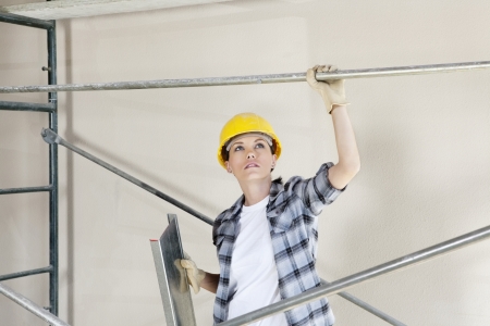 Mid adult female architect looking up while standing under scaffold at construction siteの写真素材