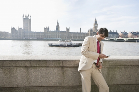 Indian businessman text messaging with watercraft and buildings in backgroundの写真素材