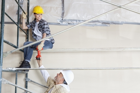 Male architect giving drill to female worker on scaffold at construction siteの写真素材