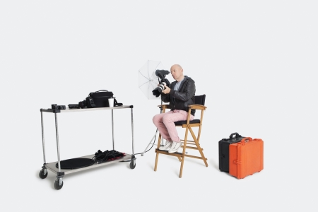 Senior photographer looking at camera while sitting on director's chair in studioの写真素材
