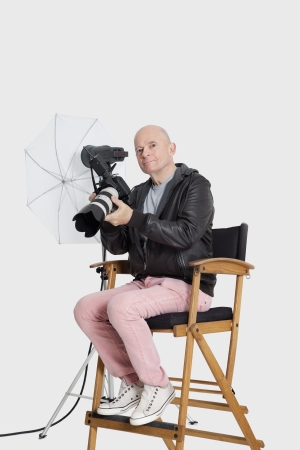 Portrait of senior photographer sitting on director's chair with cameraの写真素材