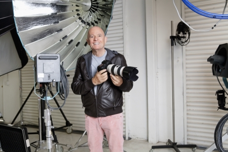 Portrait of happy senior photographer with camera in studioの写真素材