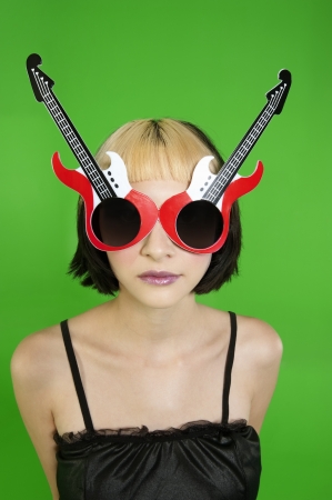 Beautiful young model with guitar shaped sunglasses over green backgroundの写真素材
