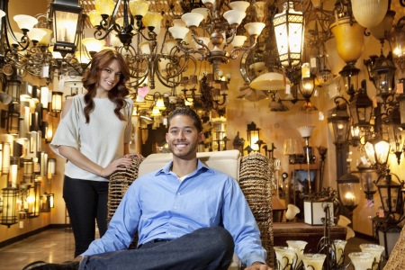 Portrait of handsome young man sitting while woman standing background in lights storeの写真素材
