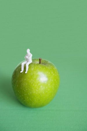 Close-up of human figurine sitting on green apple over colored backgroundの写真素材