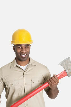 Portrait of happy African male construction worker holding axe over gray backgroundの写真素材