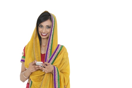 Portrait of young Indian woman in traditional wear holding cell phone against white backgroundの写真素材