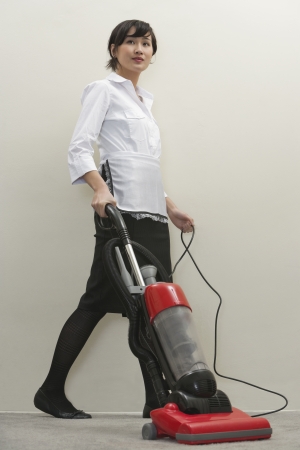 Full length of young female housekeeper vacuumingの写真素材