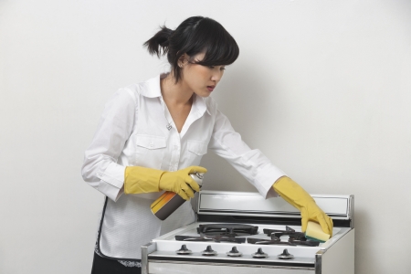 Young housemaid cleaning stove against gray backgroundの写真素材
