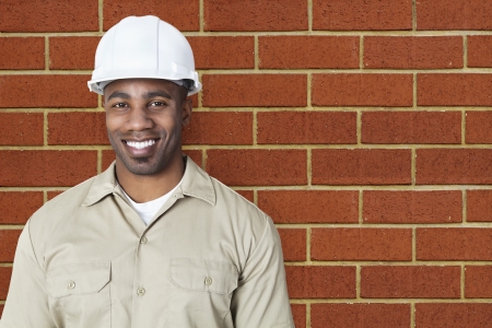 Portrait of happy young construction worker with hardhat over brick wallの写真素材