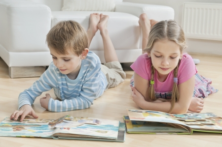 Siblings reading story books on floor in the living roomの写真素材