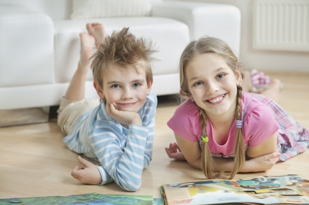 Portrait of happy siblings with story books lying on floor in living roomの写真素材