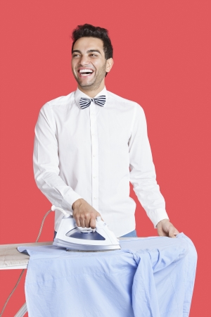 Cheerful man in formals ironing shirt over red backgroundの写真素材
