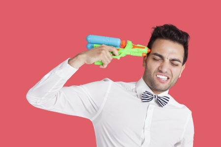 Frustrated man holding toy gun to his head over red backgroundの写真素材