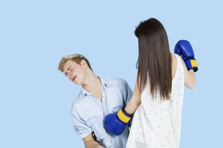 Young female boxer punching man over blue background