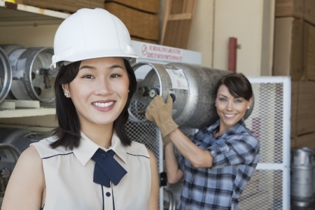 Portrait of woman smiling with female industrial worker carrying propane cylinder in backgroundの写真素材