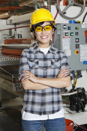 Portrait of happy Asian female industrial worker with machinery in backgroundの写真素材