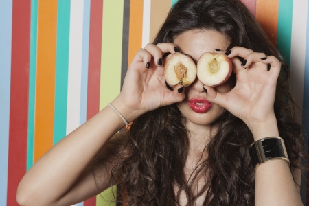 Young woman covering her eyes with peach against striped backgroundの写真素材