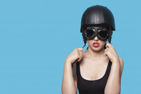 Young woman wearing nostalgic helmet and goggles against blue backgroundの写真素材