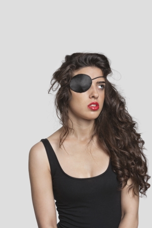 Thoughtful young woman wearing eye patch over gray backgroundの写真素材