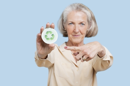 Portrait of senior woman holding badge with recycling symbol against blue backgroundの写真素材