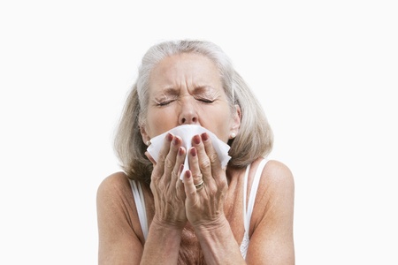 Senior woman sneezing into a tissue against white backgroundの写真素材