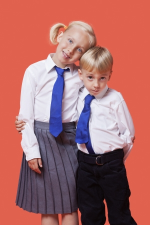 Portrait of young siblings in school uniform with arm around over orange backgroundの写真素材