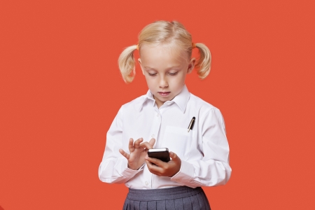 Young school girl reading text messages over orange backgroundの写真素材